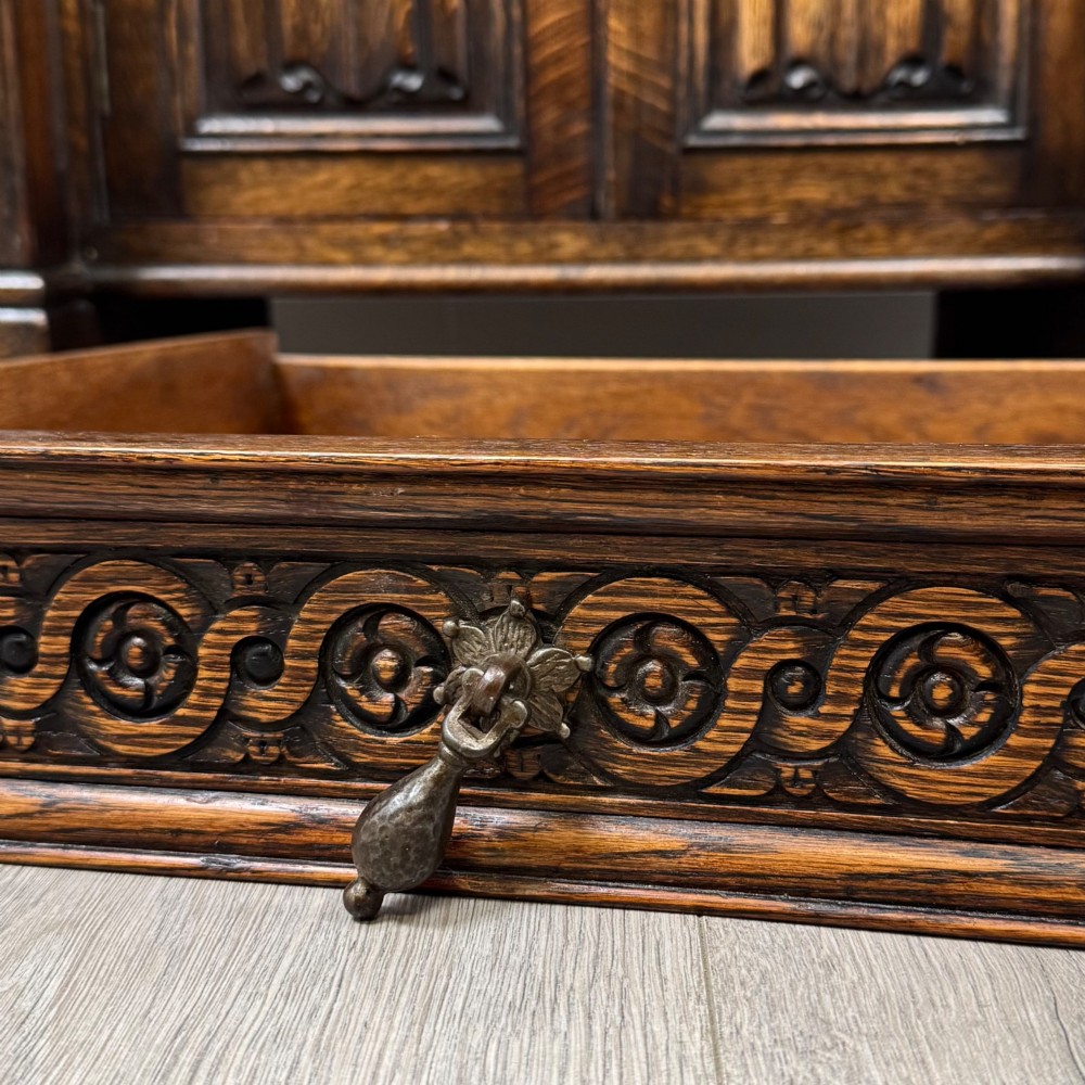 A dark carved oak Edwardian kneehole desk featuring frieze drawers with carved detailing and lower cupboard doors with vertical carved panels. View XII