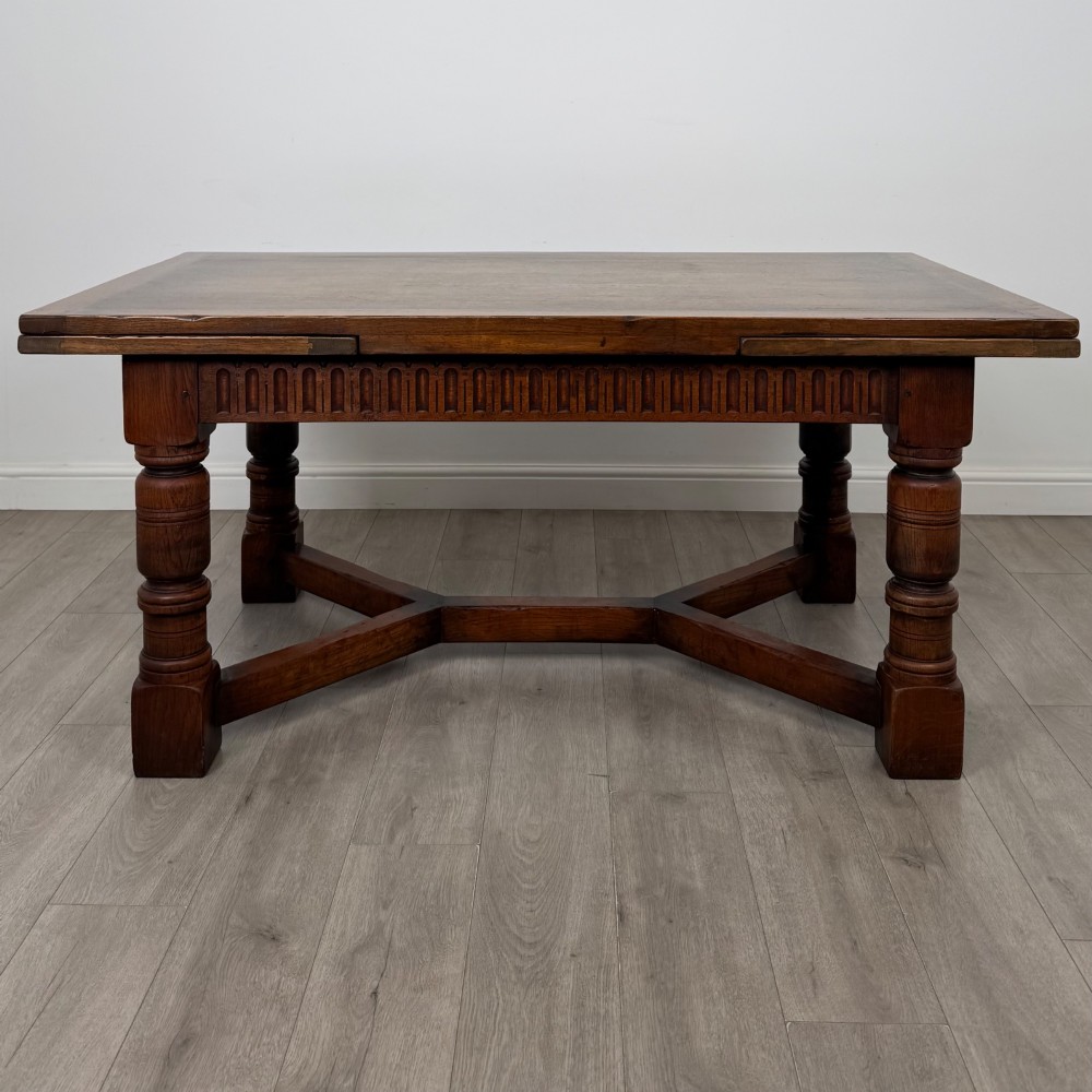 An Edwardian oak draw leaf dining table featuring extended end leaves, carved frieze aprons, heavy turned legs, and an X-form stretcher. View III