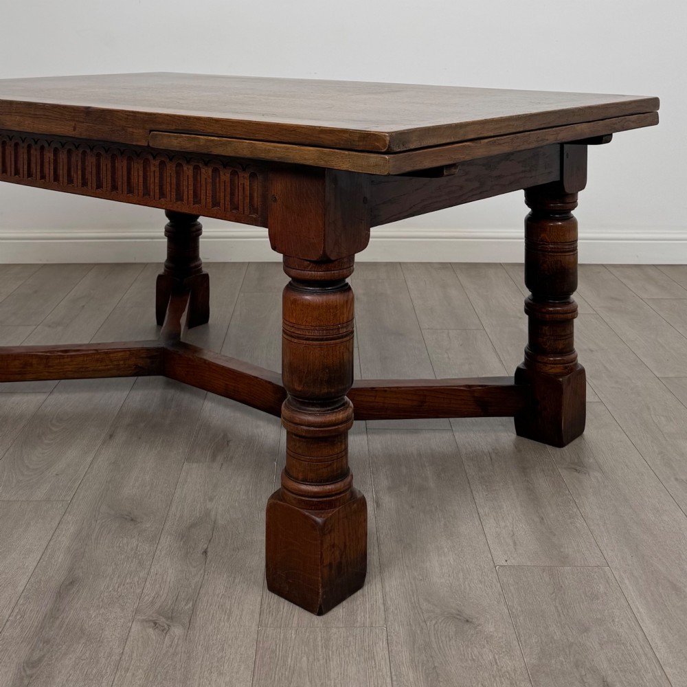 An Edwardian oak draw leaf dining table featuring extended end leaves, carved frieze aprons, heavy turned legs, and an X-form stretcher. View VI