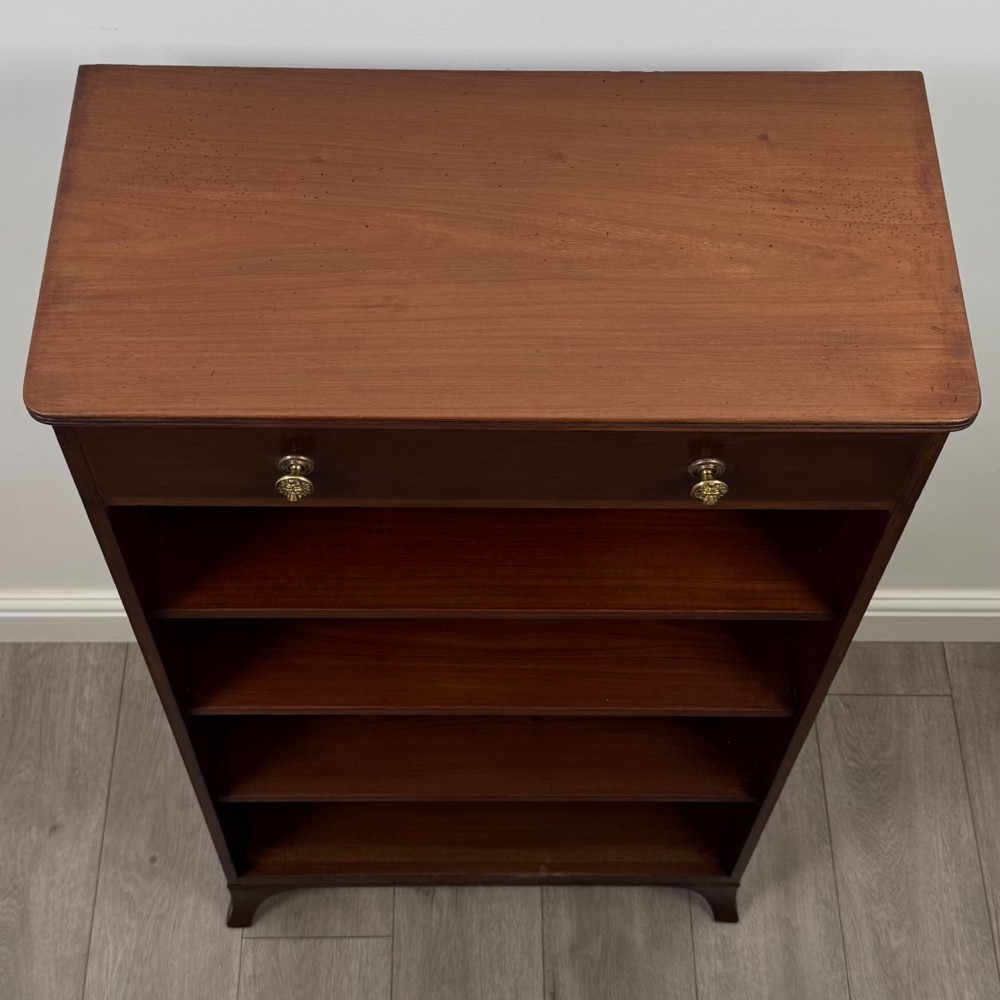 A tall 19th-century Regency mahogany open bookcase featuring four open shelves, a top drawer with twin brass knobs, and flared feet. View X