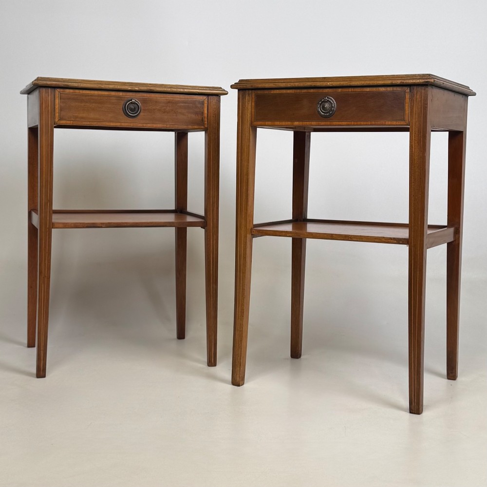 A pair of tall, slim mahogany bedside tables with single top drawers, round brass ring handles, open lower shelves, and tapered legs.