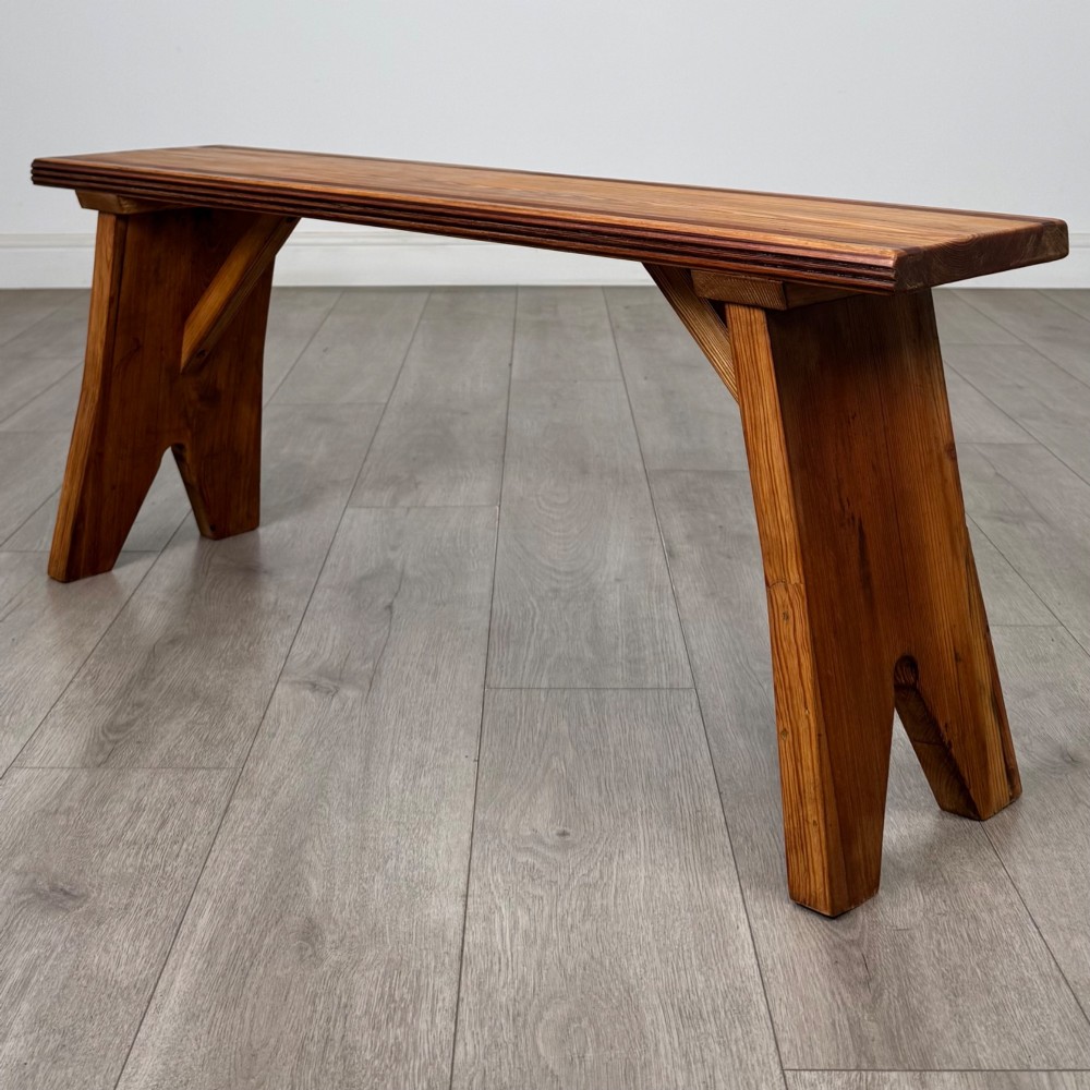 A pitch pine wooden bench with angled trestle legs, diagonal side braces, and a reeded edge along the top rectangular seat.