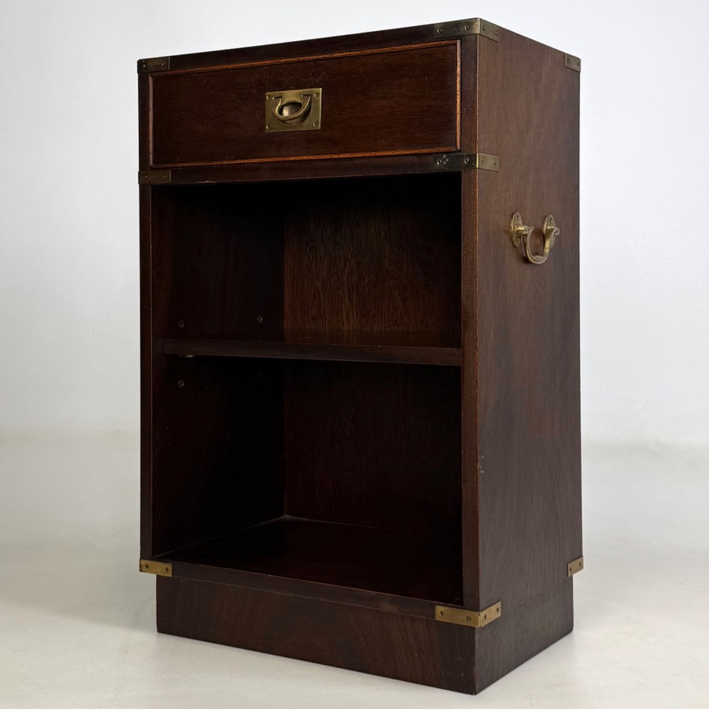 A dark mahogany campaign style cabinet featuring a single upper drawer with a flush brass handle, brass corner mounts, and two open lower shelves. View III