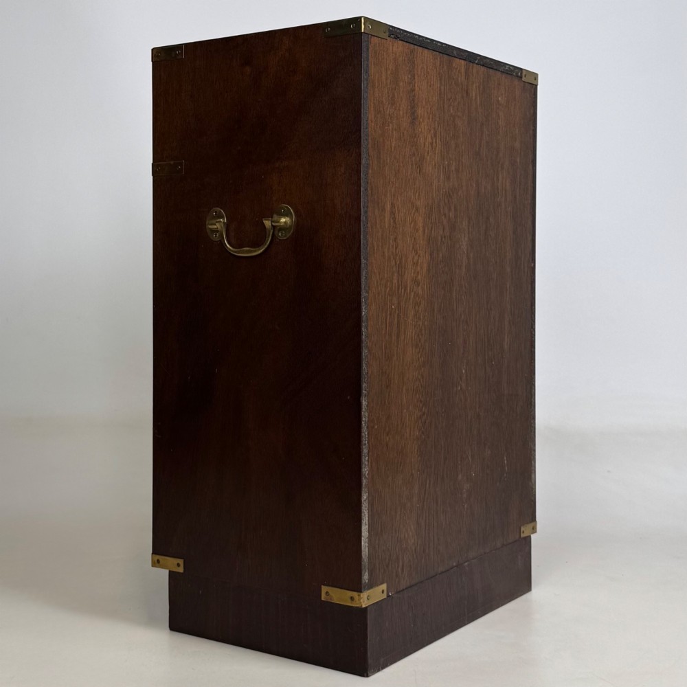 A dark mahogany campaign style cabinet featuring a single upper drawer with a flush brass handle, brass corner mounts, and two open lower shelves. View V