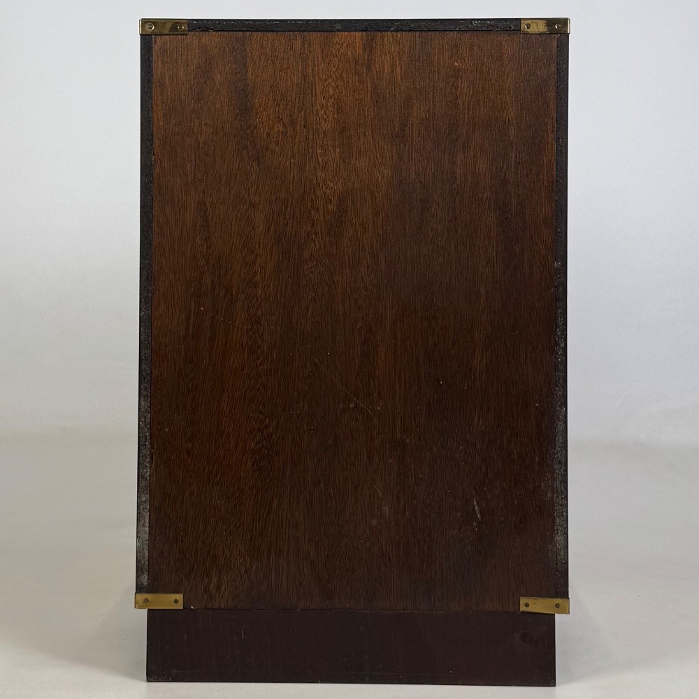 A dark mahogany campaign style cabinet featuring a single upper drawer with a flush brass handle, brass corner mounts, and two open lower shelves. View VI