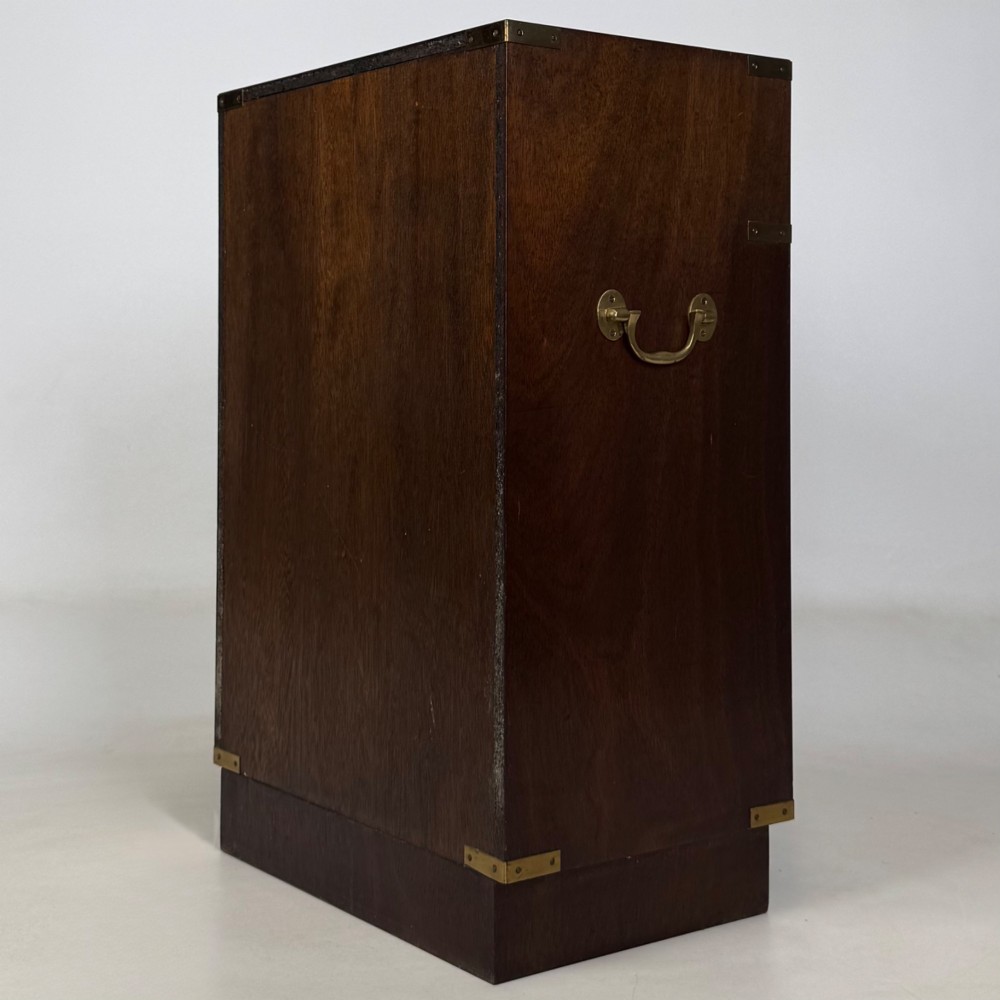 A dark mahogany campaign style cabinet featuring a single upper drawer with a flush brass handle, brass corner mounts, and two open lower shelves. View VII