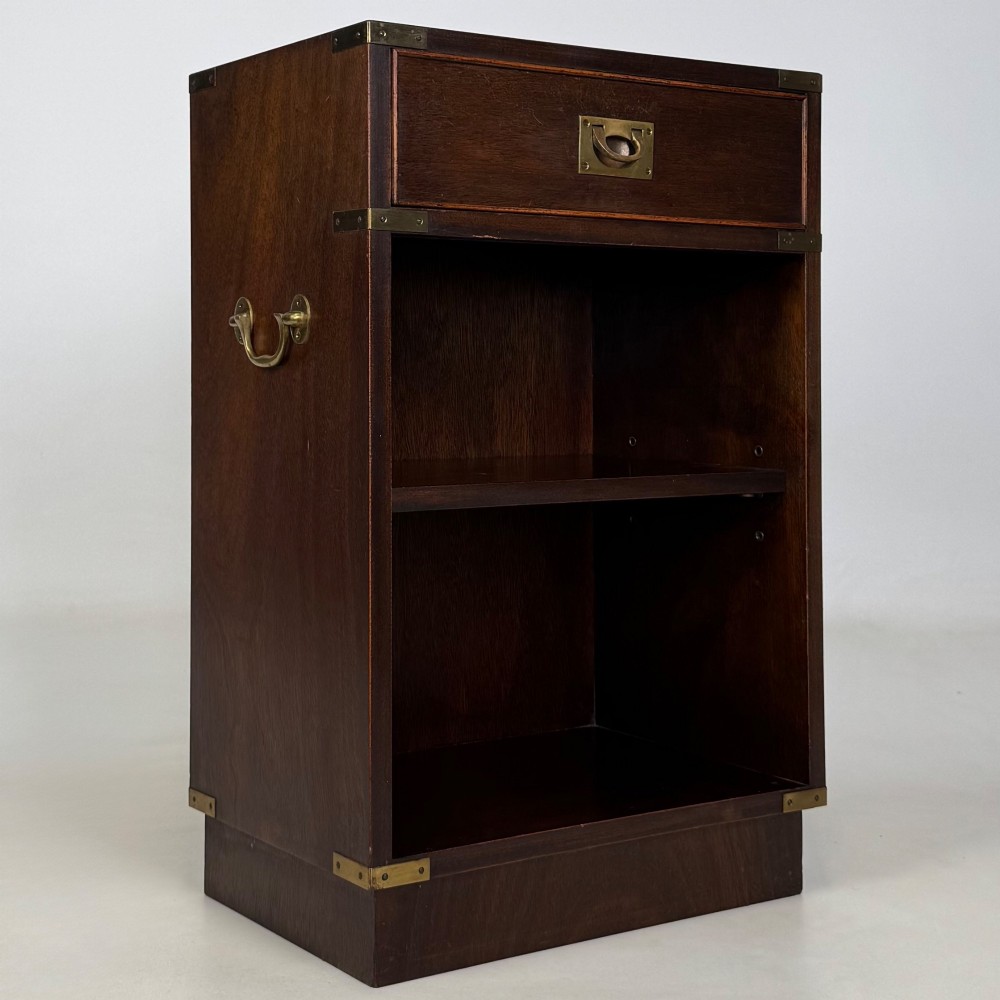 A dark mahogany campaign style cabinet featuring a single upper drawer with a flush brass handle, brass corner mounts, and two open lower shelves. View IX