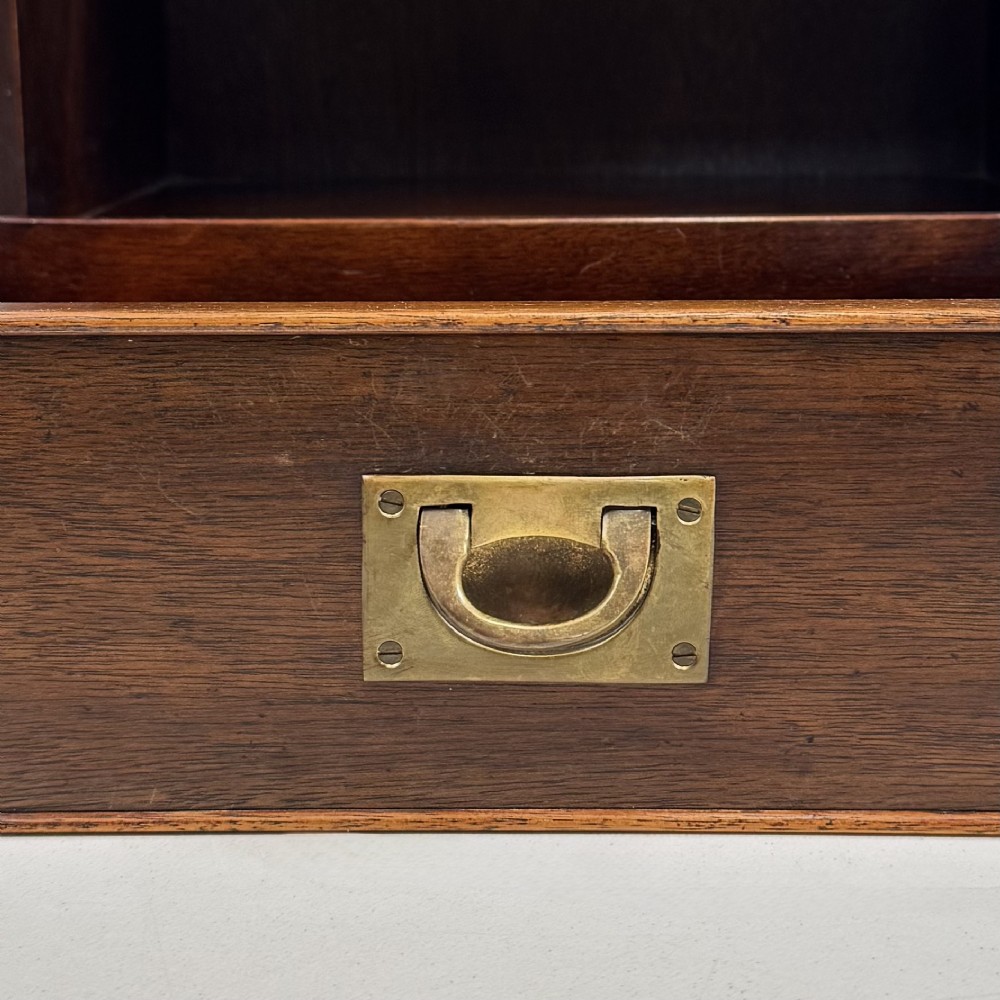 A dark mahogany campaign style cabinet featuring a single upper drawer with a flush brass handle, brass corner mounts, and two open lower shelves. View XI