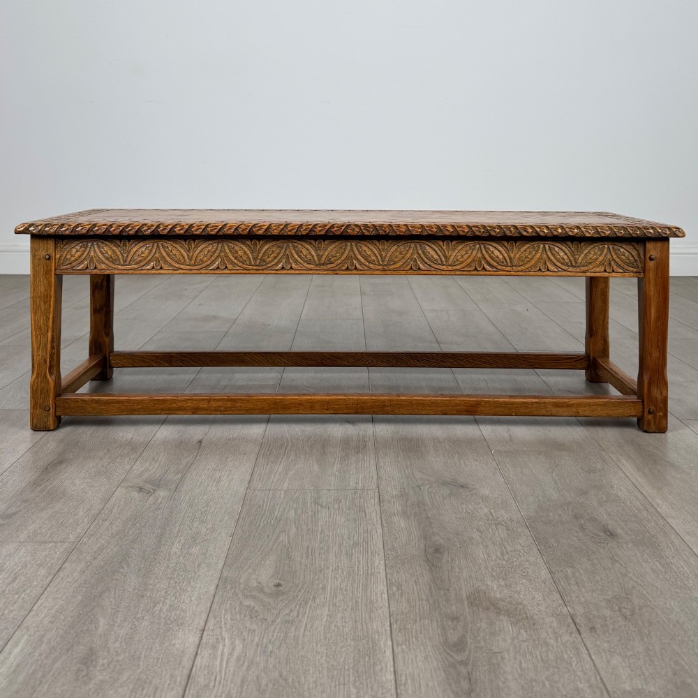 A low rectangular golden oak coffee table featuring carved leaf patterns along the apron and edges, supported by straight legs with a lower stretcher frame.