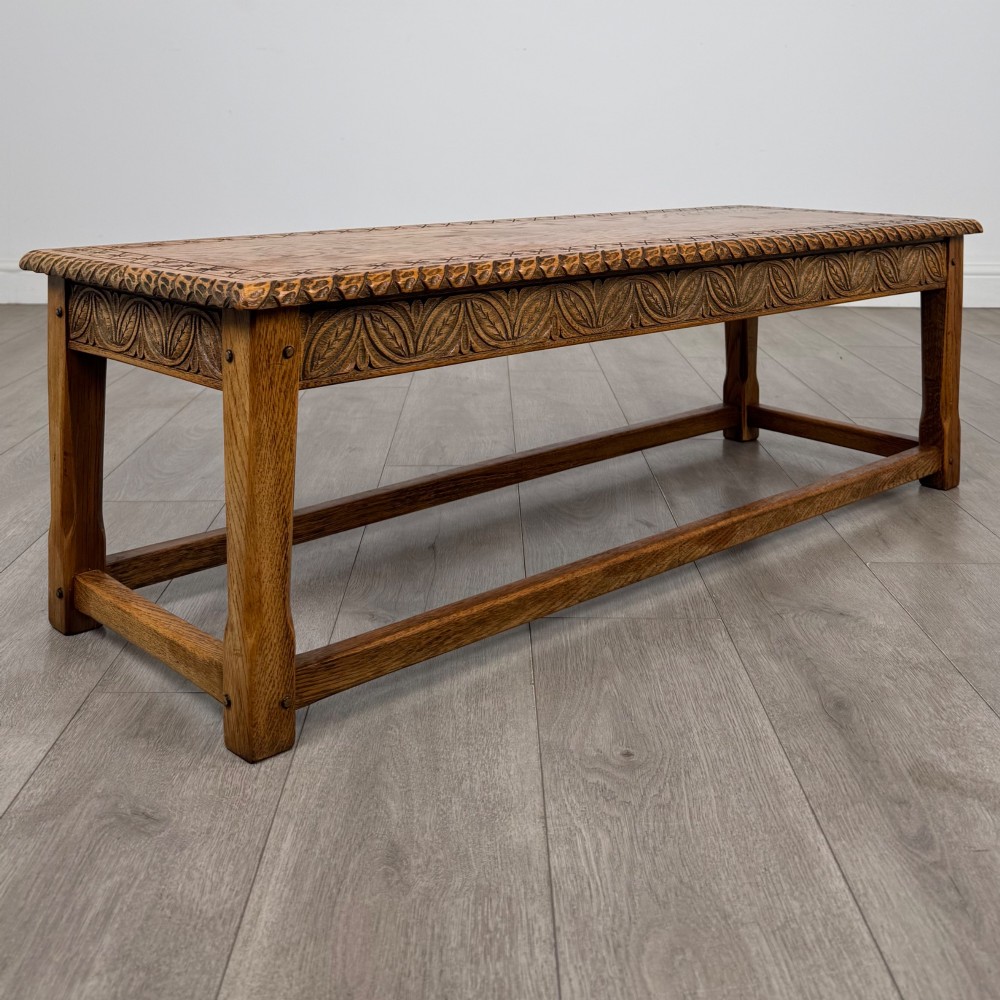A low rectangular golden oak coffee table featuring carved leaf patterns along the apron and edges, supported by straight legs with a lower stretcher frame. View IV