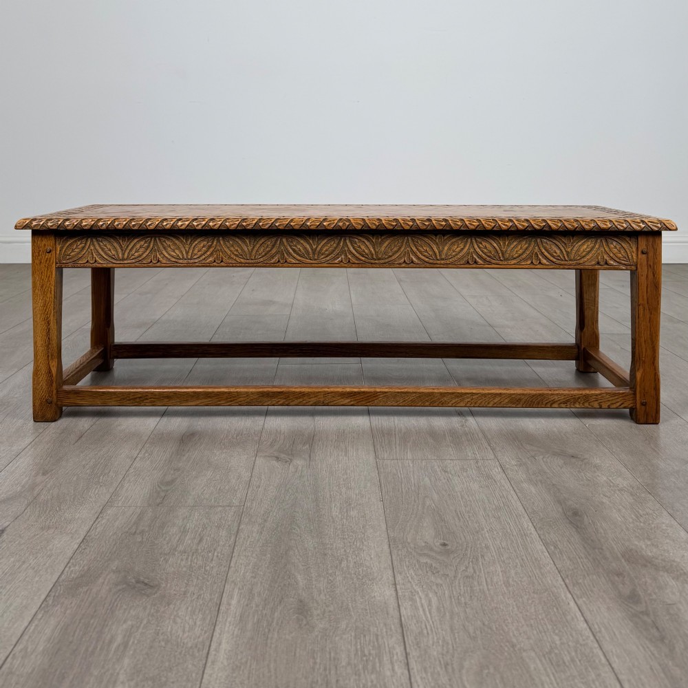A low rectangular golden oak coffee table featuring carved leaf patterns along the apron and edges, supported by straight legs with a lower stretcher frame. View V