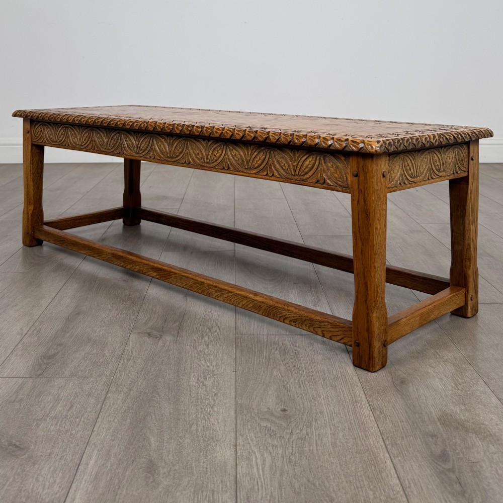 A low rectangular golden oak coffee table featuring carved leaf patterns along the apron and edges, supported by straight legs with a lower stretcher frame. View VI