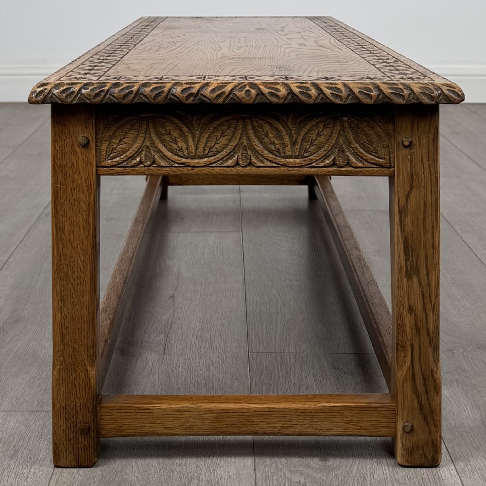 A low rectangular golden oak coffee table featuring carved leaf patterns along the apron and edges, supported by straight legs with a lower stretcher frame. View VII