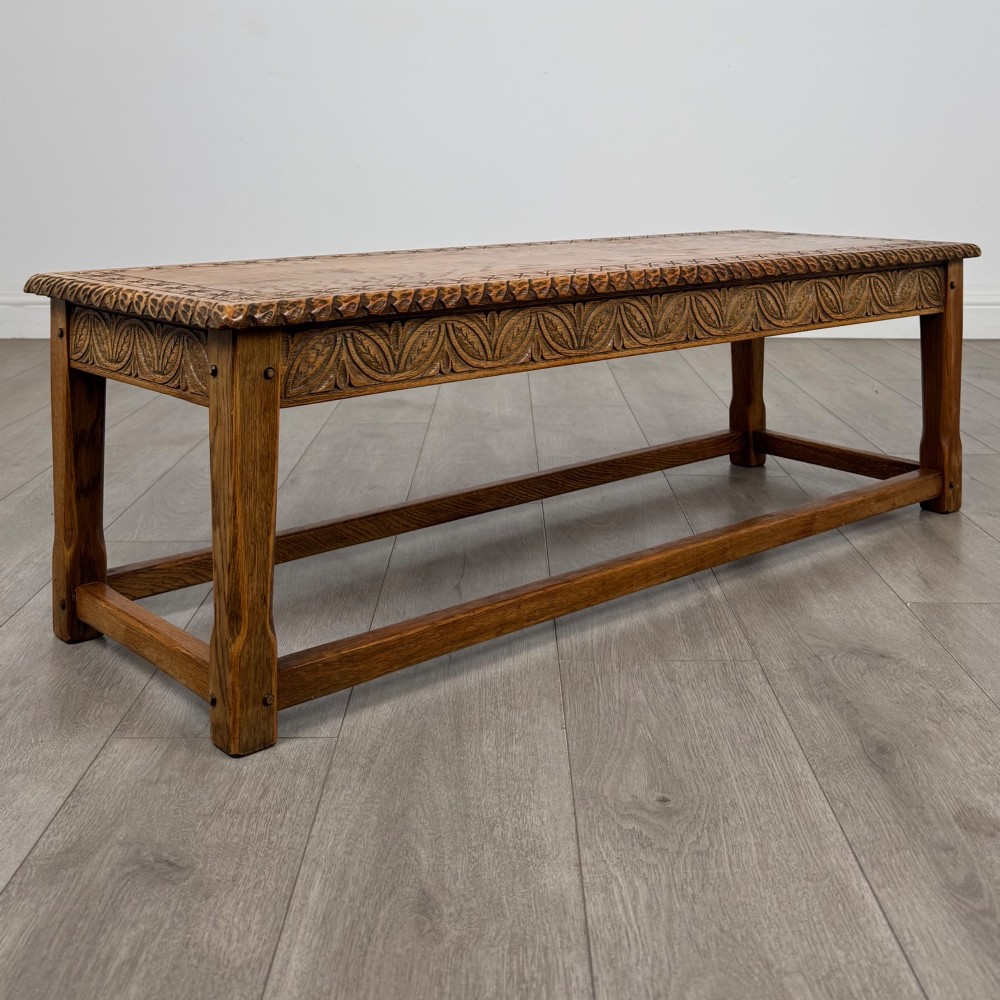 A low rectangular golden oak coffee table featuring carved leaf patterns along the apron and edges, supported by straight legs with a lower stretcher frame. View VIII