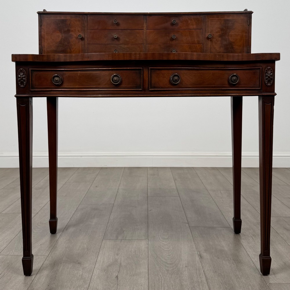 A mahogany writing table featuring a raised superstructure with small drawers and side cupboards above two main frieze drawers, supported by square tapered fluted legs.