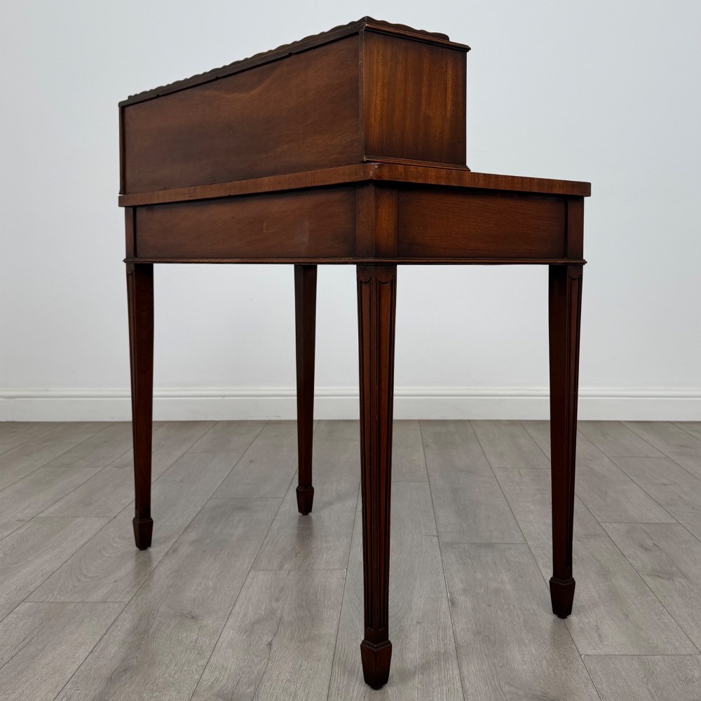 A mahogany writing table featuring a raised superstructure with small drawers and side cupboards above two main frieze drawers, supported by square tapered fluted legs. View VI
