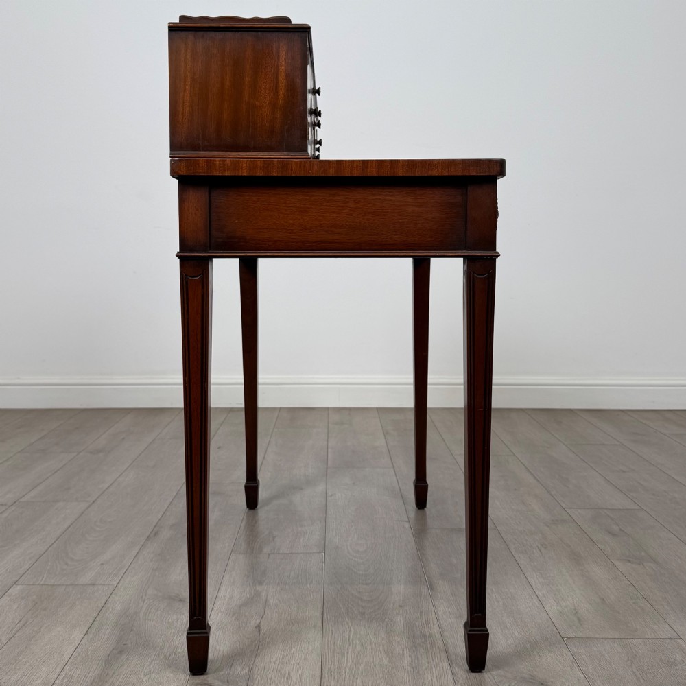 A mahogany writing table featuring a raised superstructure with small drawers and side cupboards above two main frieze drawers, supported by square tapered fluted legs. View VII