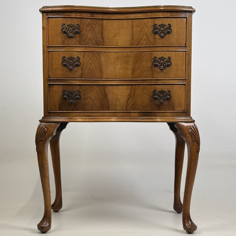 A small 20th-century walnut chest featuring three drawers, brass handles, and tall carved cabriole legs.