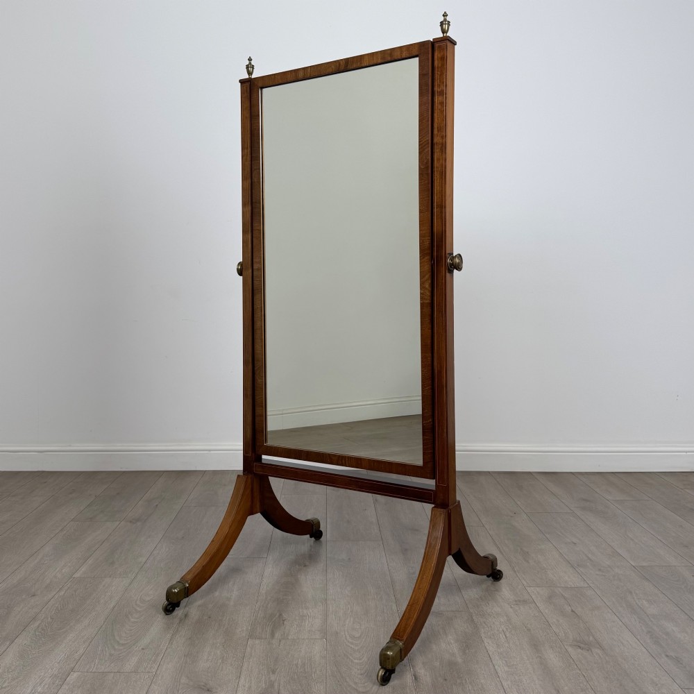 An Edwardian mahogany cheval mirror featuring a rectangular tilting mirror frame set between twin uprights with finials and splayed legs on brass castors.