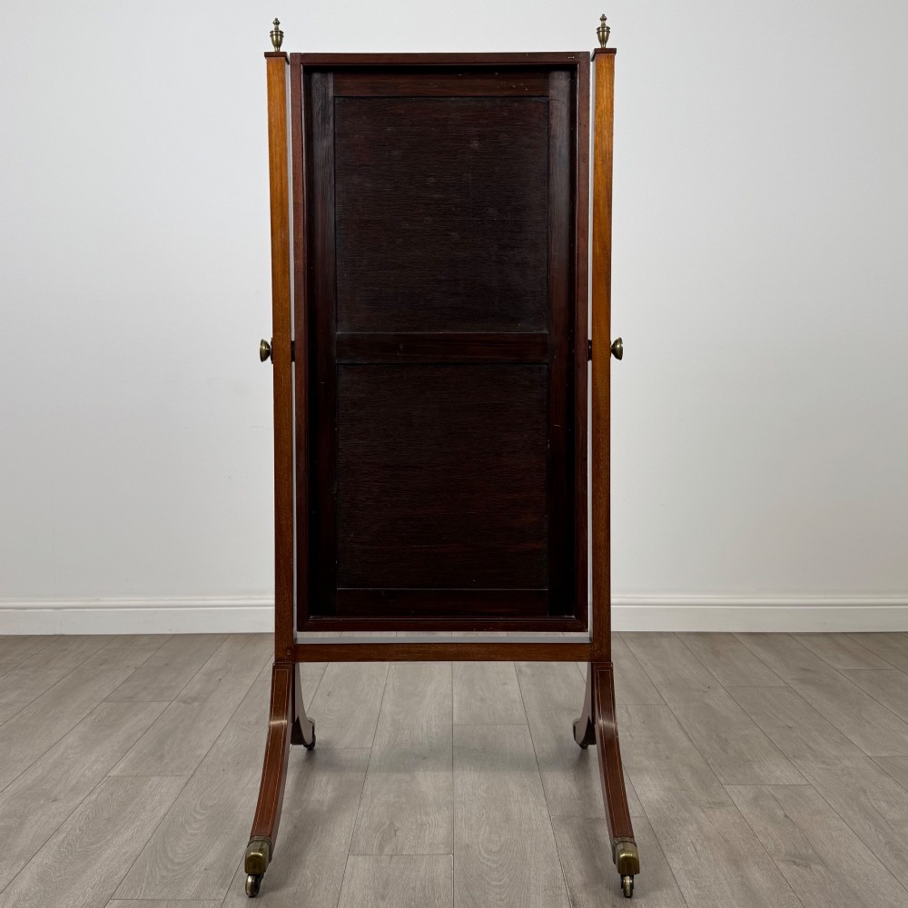 An Edwardian mahogany cheval mirror featuring a rectangular tilting mirror frame set between twin uprights with finials and splayed legs on brass castors. View V