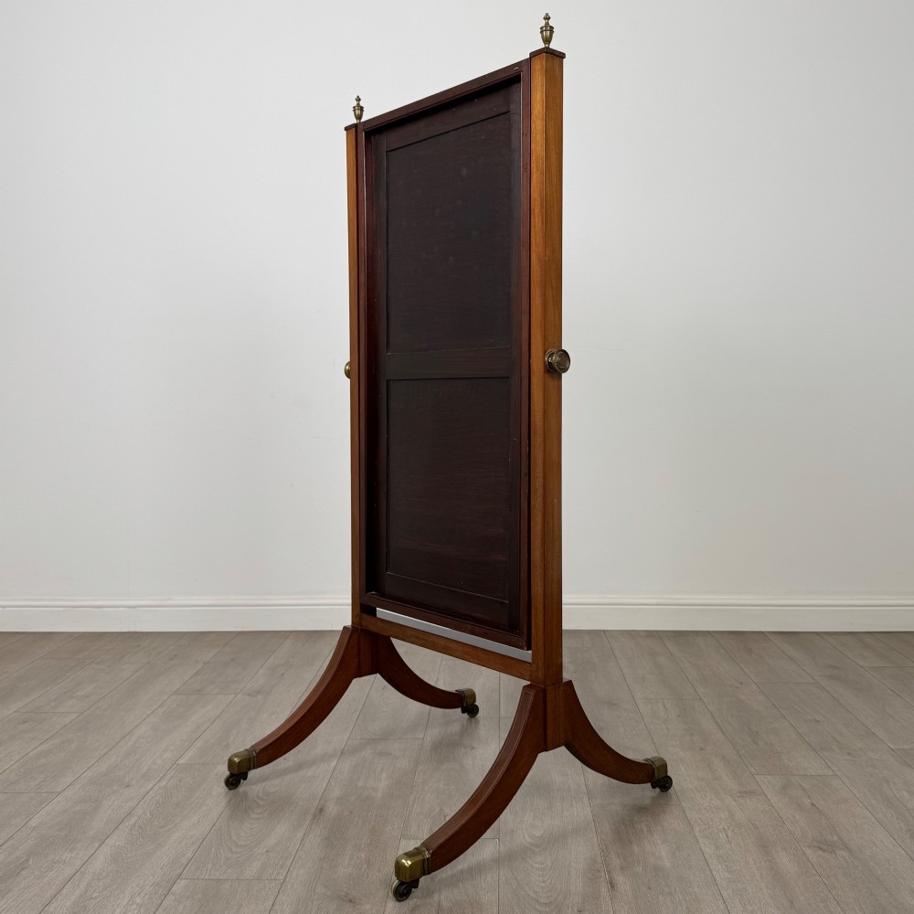 An Edwardian mahogany cheval mirror featuring a rectangular tilting mirror frame set between twin uprights with finials and splayed legs on brass castors. View VI