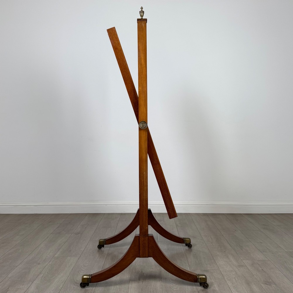 An Edwardian mahogany cheval mirror featuring a rectangular tilting mirror frame set between twin uprights with finials and splayed legs on brass castors. View VIII