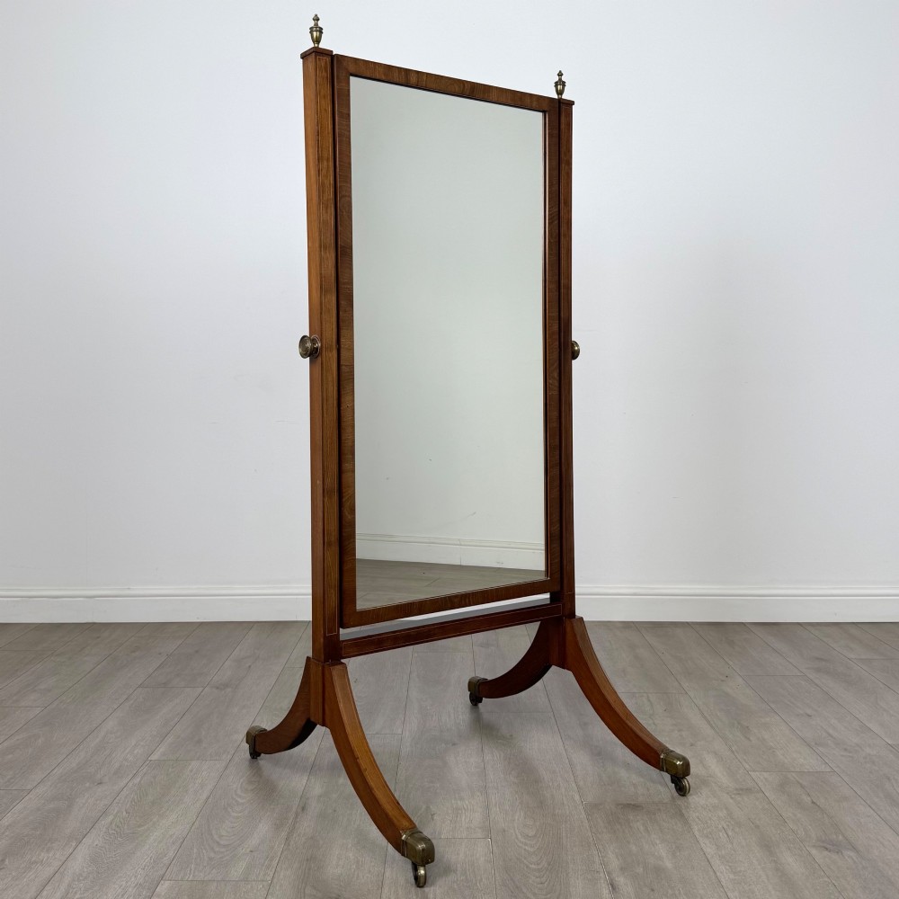 An Edwardian mahogany cheval mirror featuring a rectangular tilting mirror frame set between twin uprights with finials and splayed legs on brass castors. View IX
