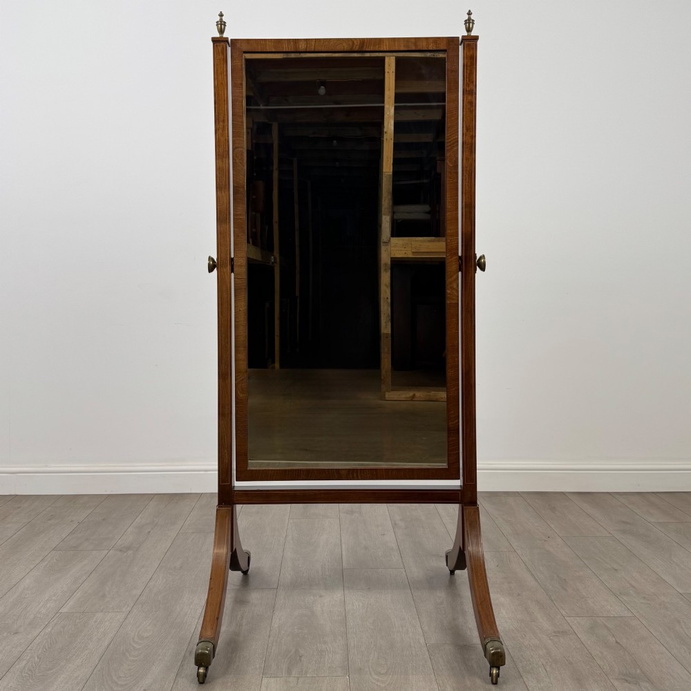 An Edwardian mahogany cheval mirror featuring a rectangular tilting mirror frame set between twin uprights with finials and splayed legs on brass castors. View X