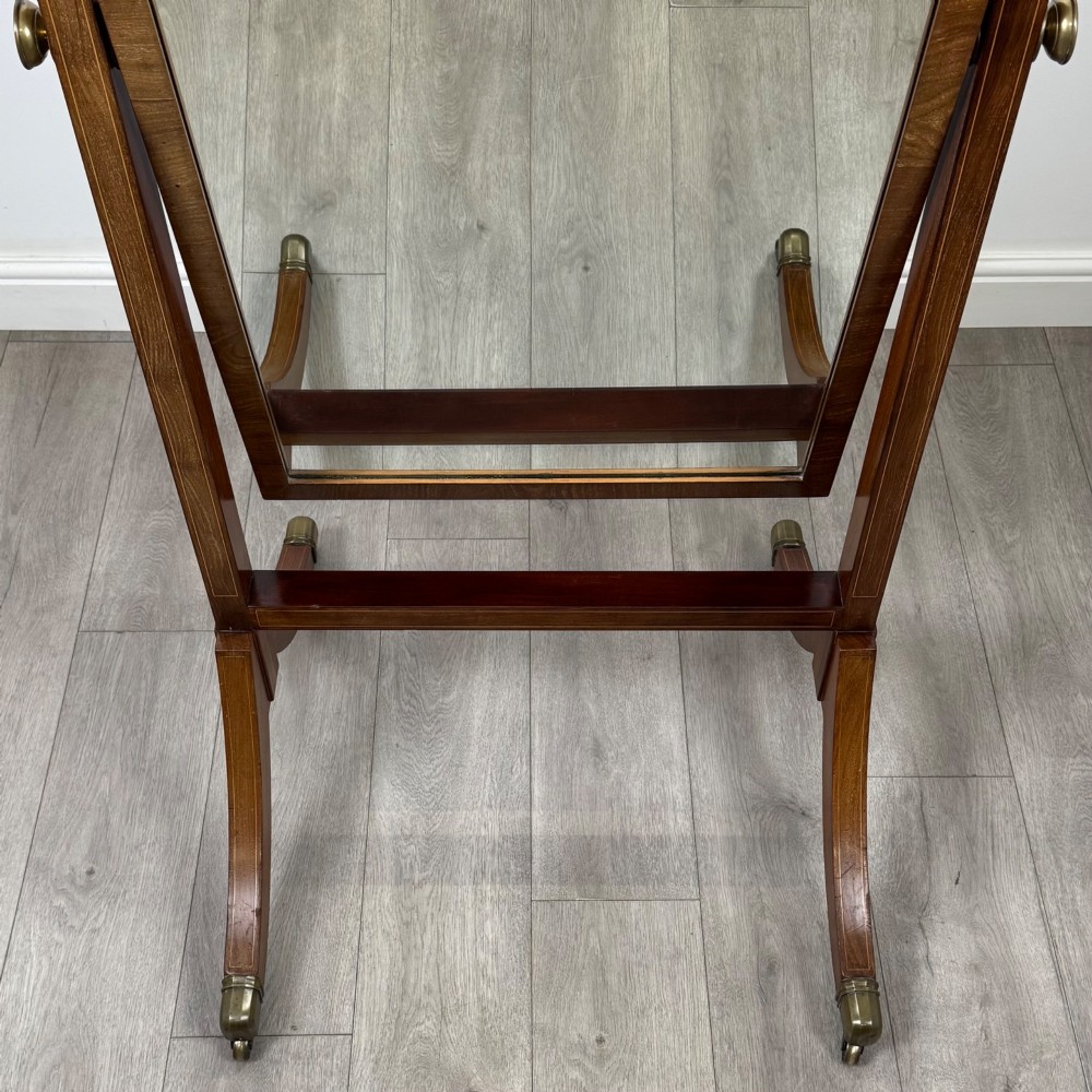 An Edwardian mahogany cheval mirror featuring a rectangular tilting mirror frame set between twin uprights with finials and splayed legs on brass castors. View XI