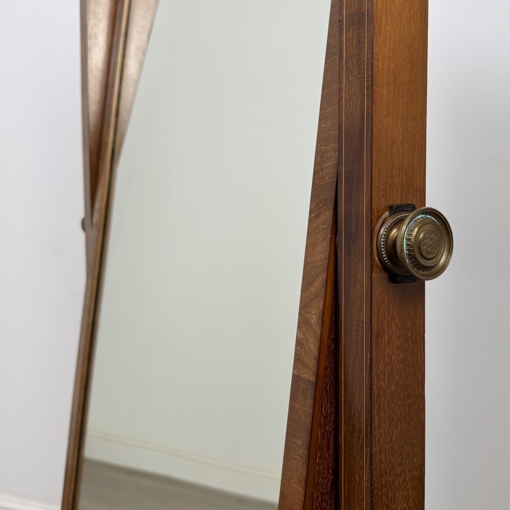 An Edwardian mahogany cheval mirror featuring a rectangular tilting mirror frame set between twin uprights with finials and splayed legs on brass castors. View XIII