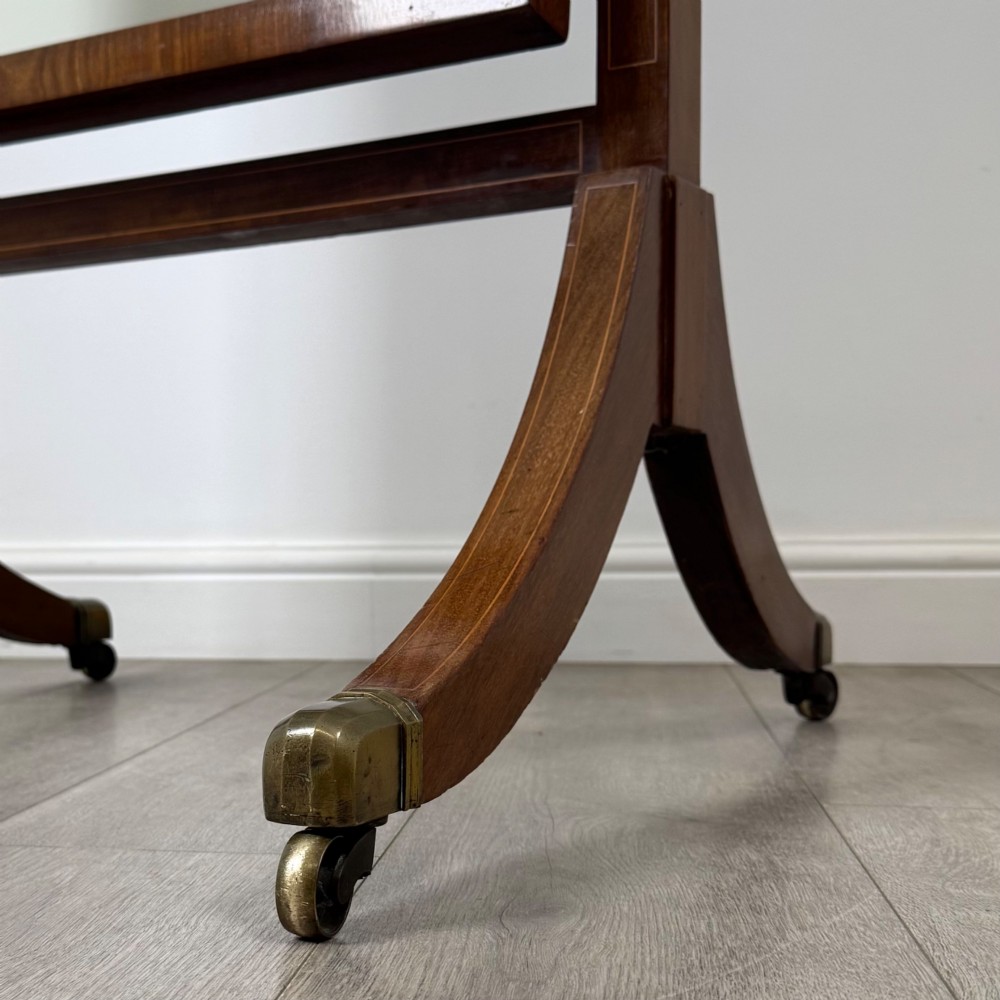 An Edwardian mahogany cheval mirror featuring a rectangular tilting mirror frame set between twin uprights with finials and splayed legs on brass castors. View XIV