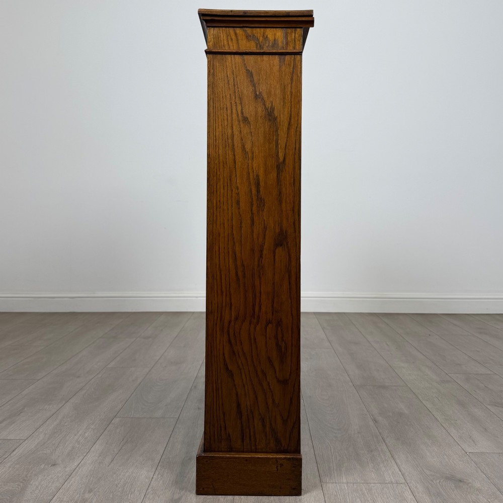 An antique Edwardian open oak bookcase featuring three wide shelves filled with red hardback books, flanked by reeded side pilasters and supported by a solid plinth base. View IV