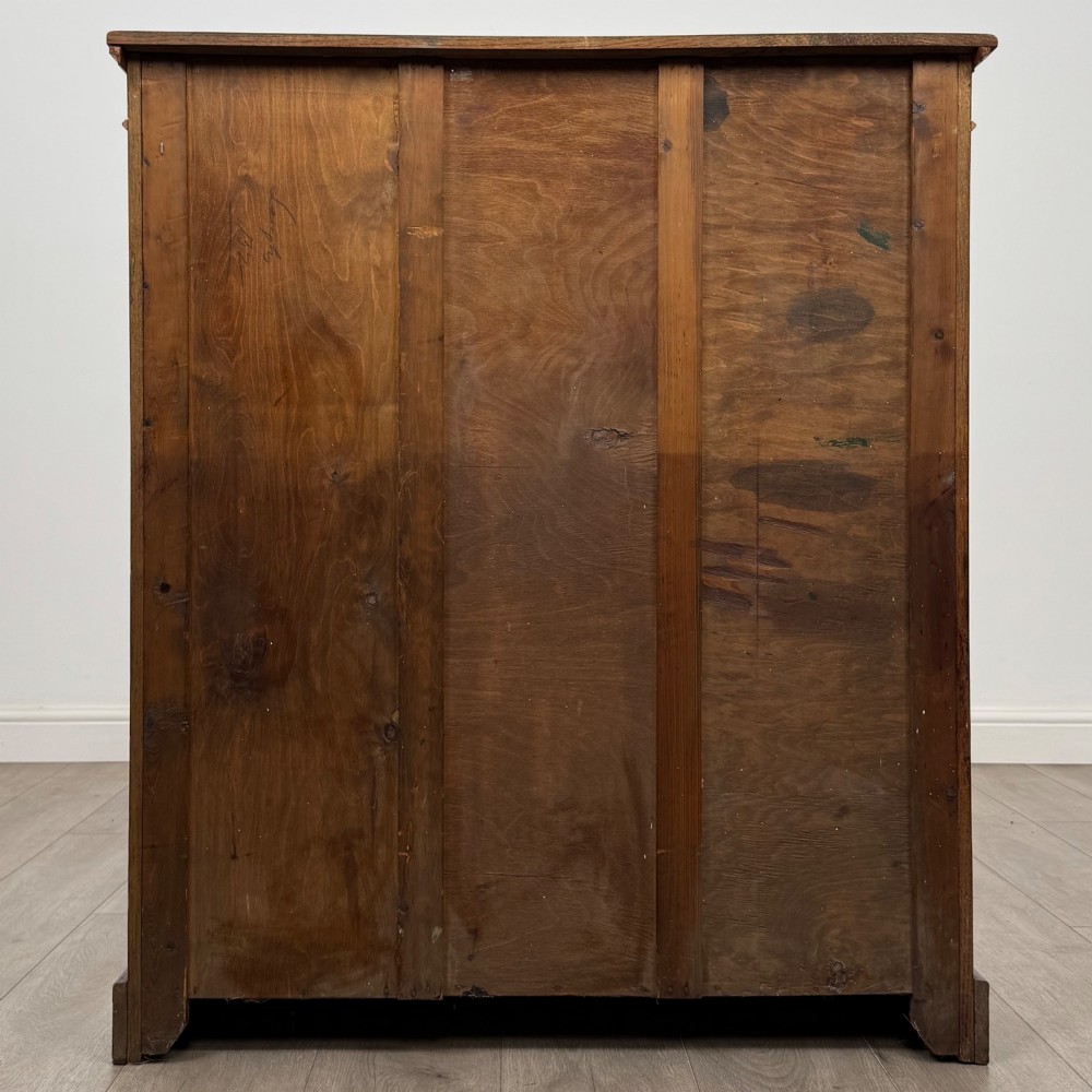 An antique Edwardian open oak bookcase featuring three wide shelves filled with red hardback books, flanked by reeded side pilasters and supported by a solid plinth base. View VI