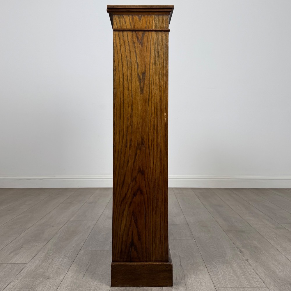An antique Edwardian open oak bookcase featuring three wide shelves filled with red hardback books, flanked by reeded side pilasters and supported by a solid plinth base. View VIII