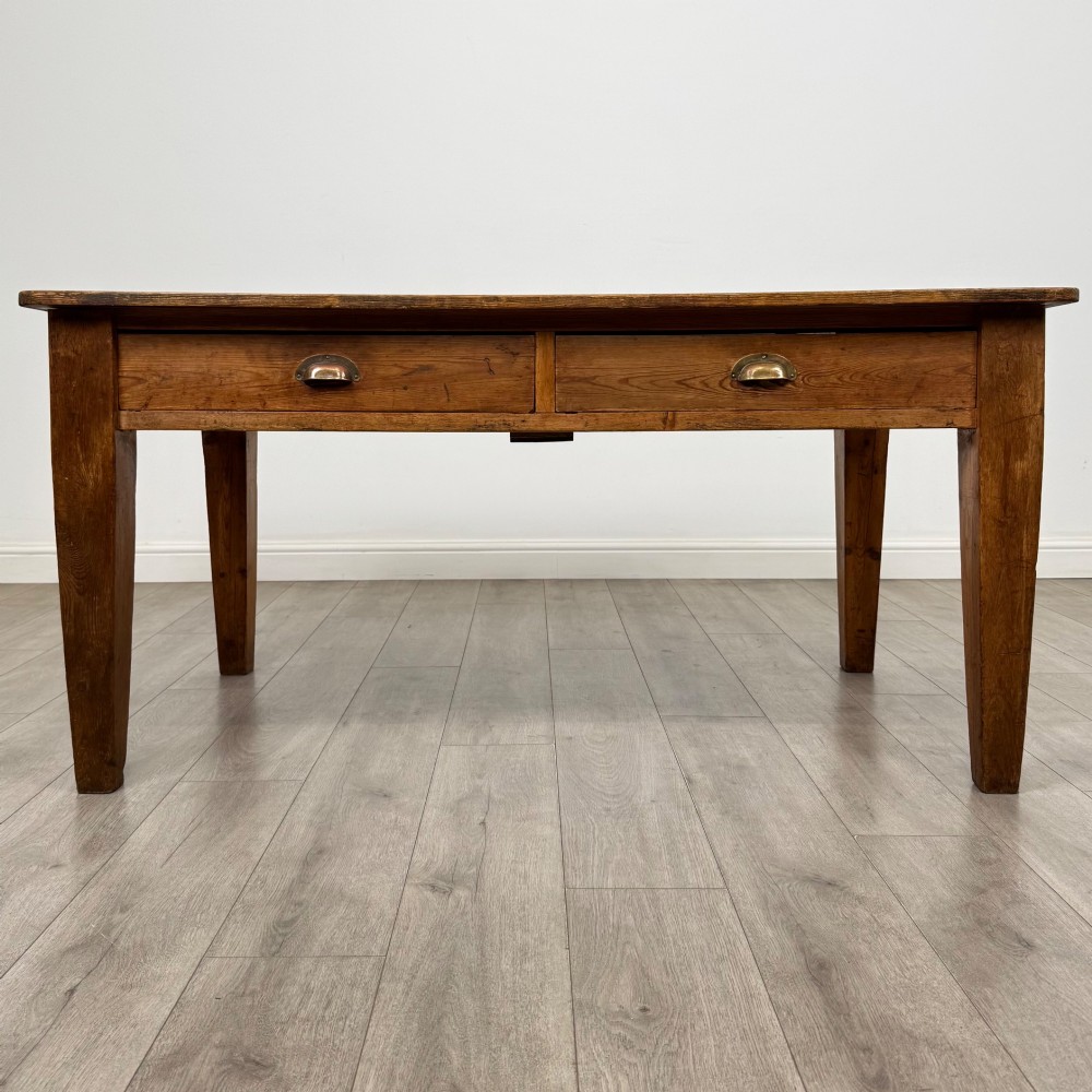 A 19th-century pine writing table featuring two front drawers with brass cup handles and tapered square legs.
