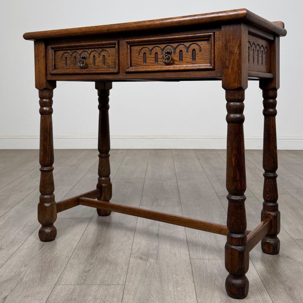 An antique Edwardian dark oak side table featuring two carved front drawers with brass ring pulls and turned legs joined by stretchers. View II