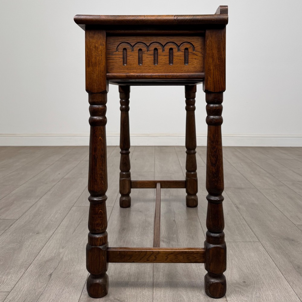 An antique Edwardian dark oak side table featuring two carved front drawers with brass ring pulls and turned legs joined by stretchers. View III