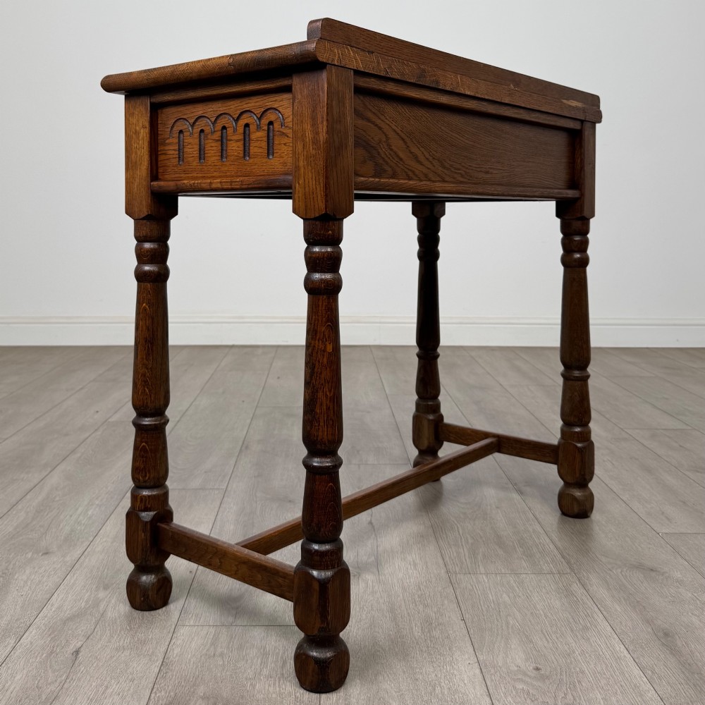 An antique Edwardian dark oak side table featuring two carved front drawers with brass ring pulls and turned legs joined by stretchers. View IV