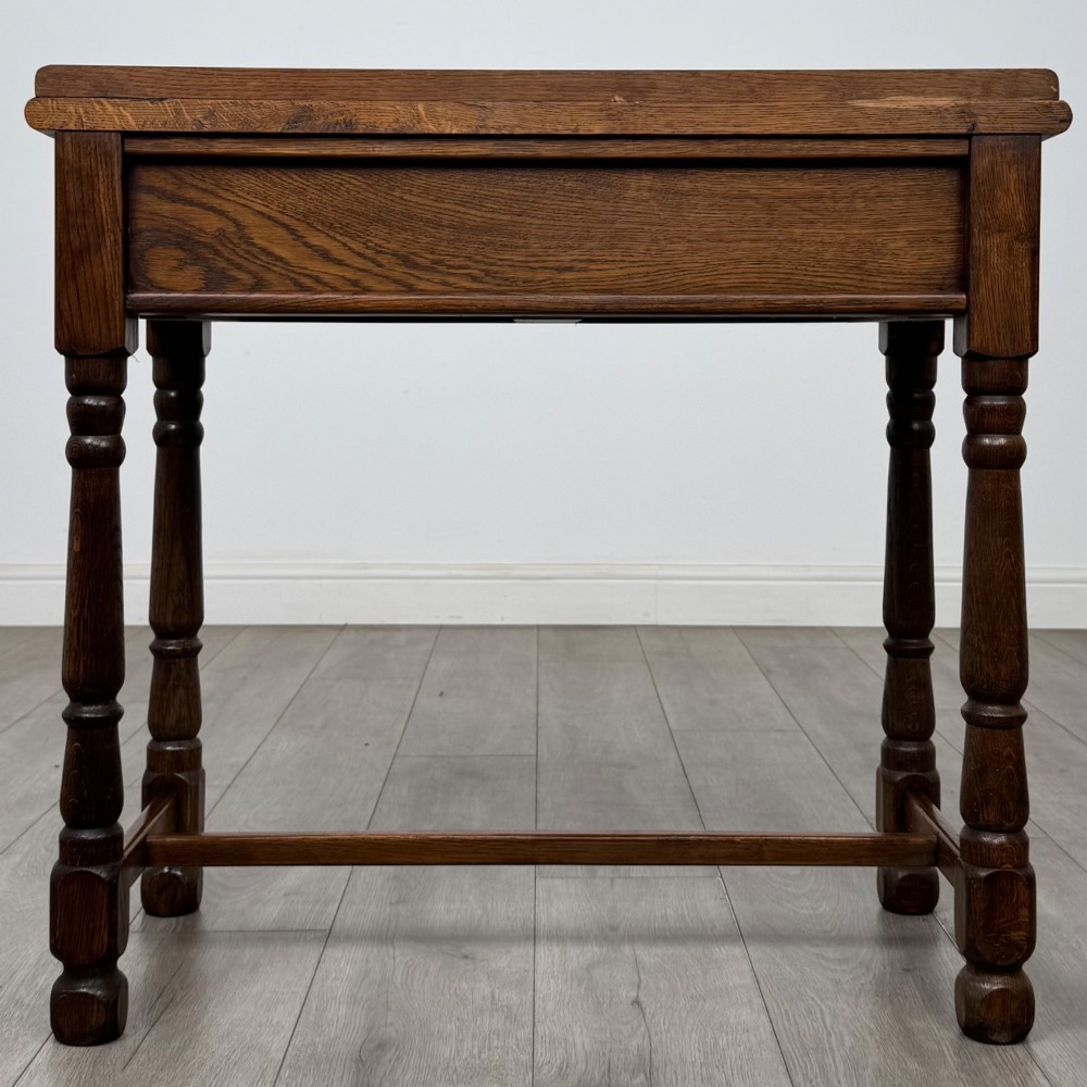 An antique Edwardian dark oak side table featuring two carved front drawers with brass ring pulls and turned legs joined by stretchers. View V