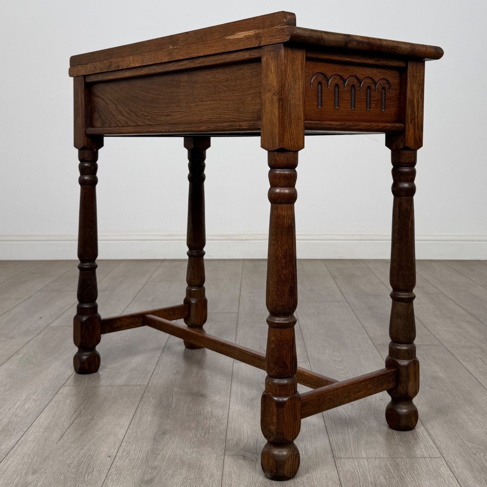 An antique Edwardian dark oak side table featuring two carved front drawers with brass ring pulls and turned legs joined by stretchers. View VI
