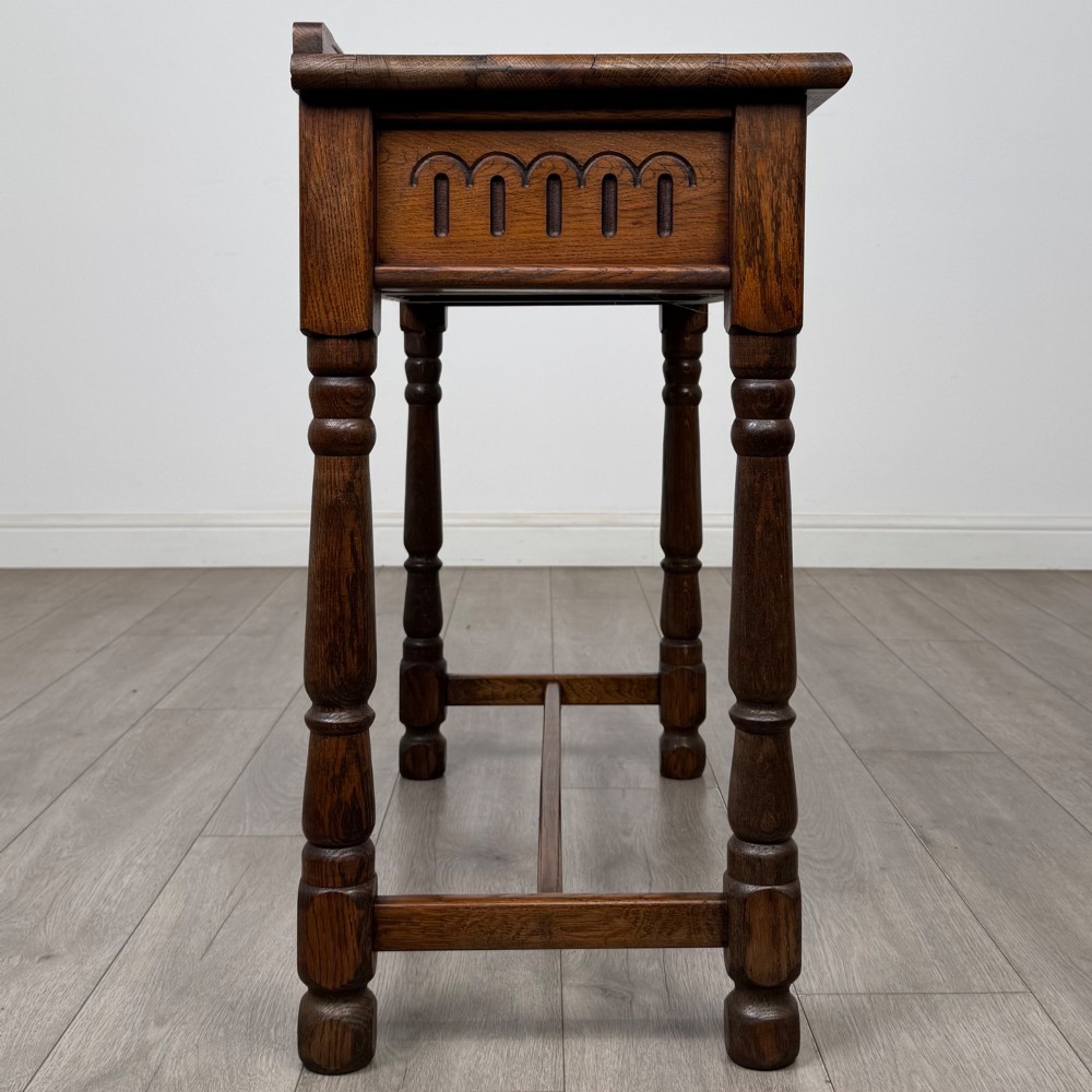 An antique Edwardian dark oak side table featuring two carved front drawers with brass ring pulls and turned legs joined by stretchers. View VII