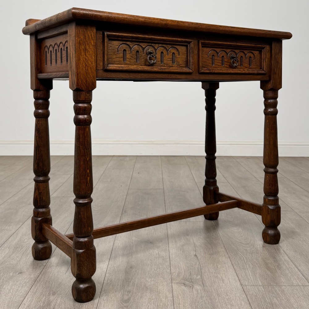 An antique Edwardian dark oak side table featuring two carved front drawers with brass ring pulls and turned legs joined by stretchers. View VIII