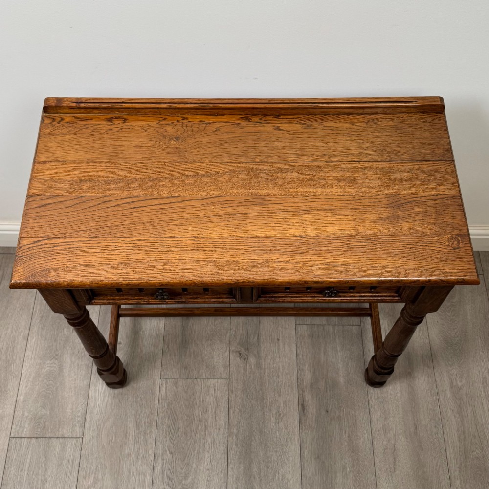 An antique Edwardian dark oak side table featuring two carved front drawers with brass ring pulls and turned legs joined by stretchers. View IX