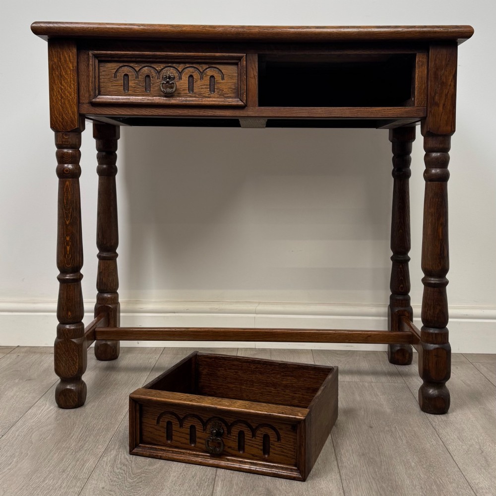 An antique Edwardian dark oak side table featuring two carved front drawers with brass ring pulls and turned legs joined by stretchers. View X