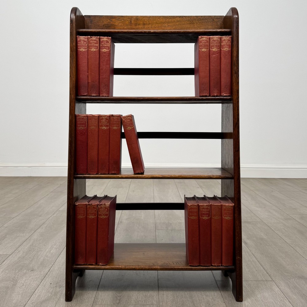 A freestanding early 20th-century warm brown open oak bookcase featuring three fixed shelves and solid side panels.