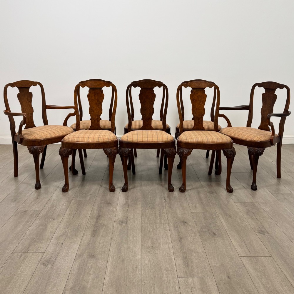 A set of eight Queen Anne revival burr walnut dining chairs featuring carved cabriole legs, claw and ball feet, vasiform splat backs, and patterned upholstered seats.
