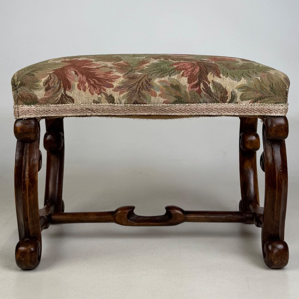 An Edwardian rectangular low stool featuring a carved dark walnut frame with scroll legs, an H-stretcher, and botanical tapestry upholstery.