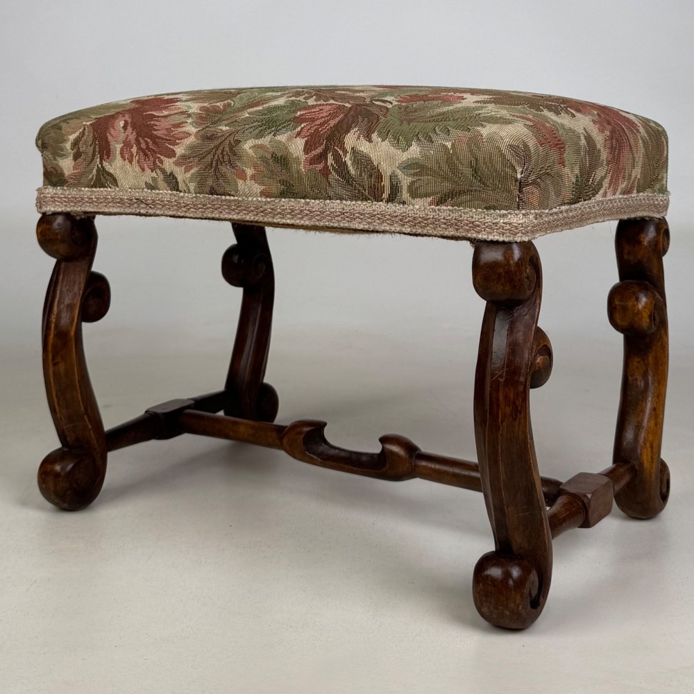 An Edwardian rectangular low stool featuring a carved dark walnut frame with scroll legs, an H-stretcher, and botanical tapestry upholstery. View II