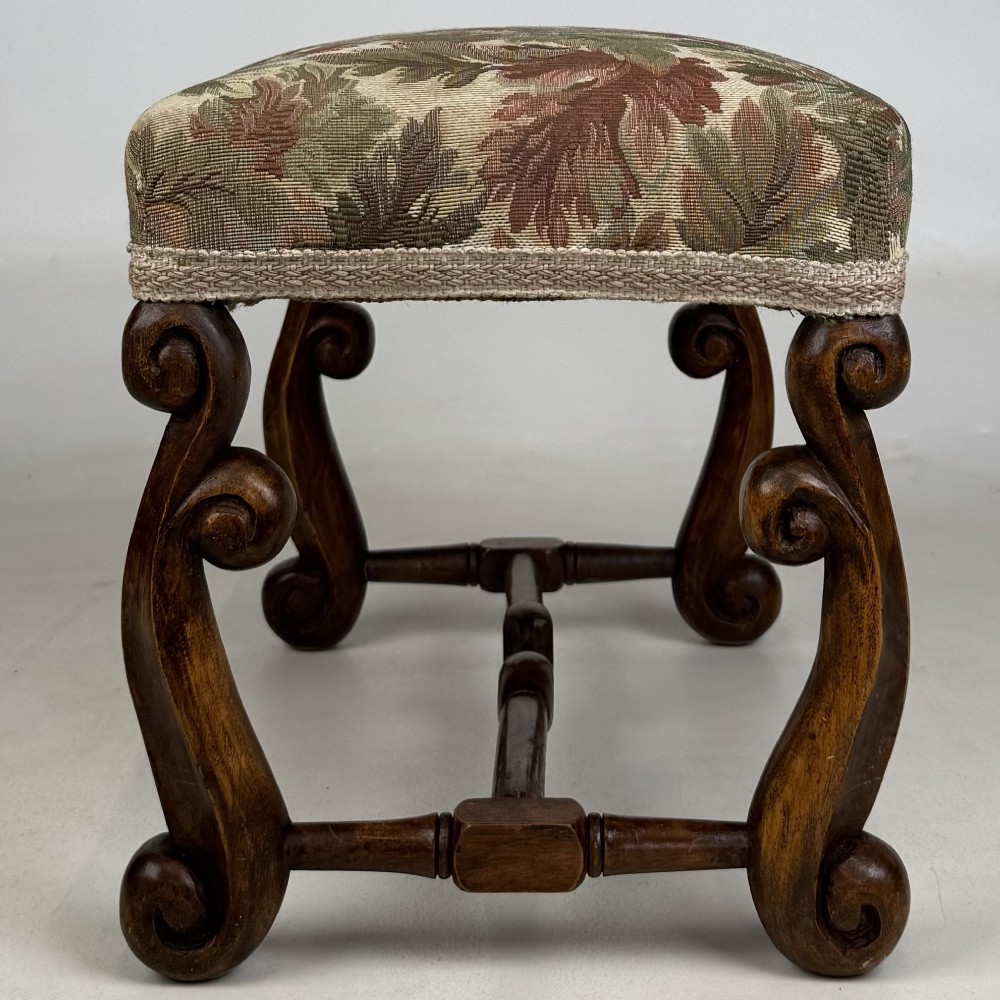 An Edwardian rectangular low stool featuring a carved dark walnut frame with scroll legs, an H-stretcher, and botanical tapestry upholstery. View III