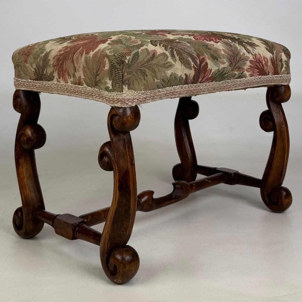 An Edwardian rectangular low stool featuring a carved dark walnut frame with scroll legs, an H-stretcher, and botanical tapestry upholstery. View IV